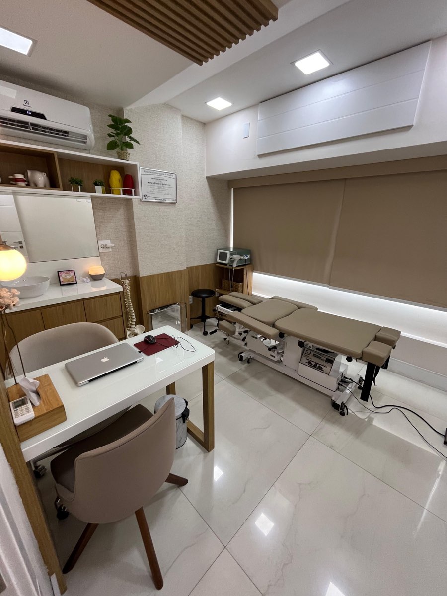 Sala de tratamento da clínica com maca de flexo-distração e mesa de avaliação